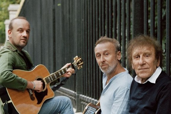 Alain Souchon et ses fils assis sur un muret, guitare en main