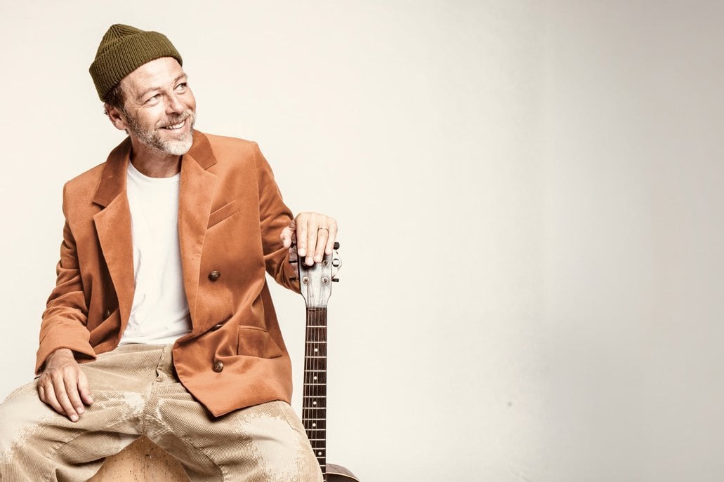 Christophe Maé assis, une guitare à ses côtés