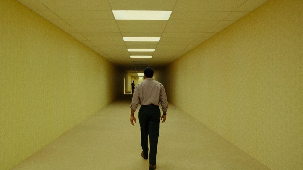 Chiwetel Ejiofor, de dos, avance seul dans un long couloir jaunâtre éclairé par des néons, dans Backrooms de Kane Parsons