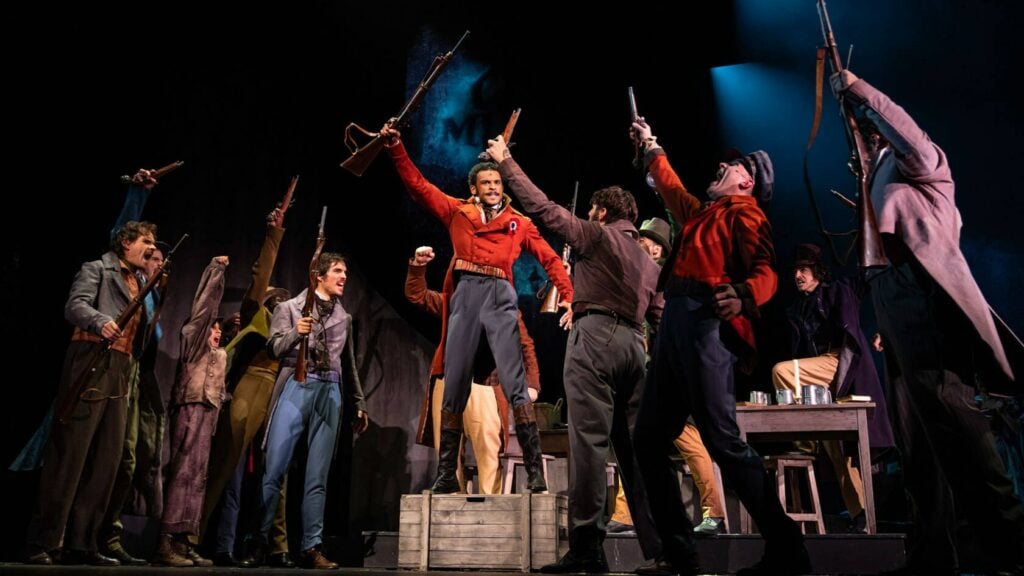 Les étudiants révolutionnaires brandissent leurs fusils autour d'Enjolras en veste rouge, sur la scène du Théâtre du Châtelet
