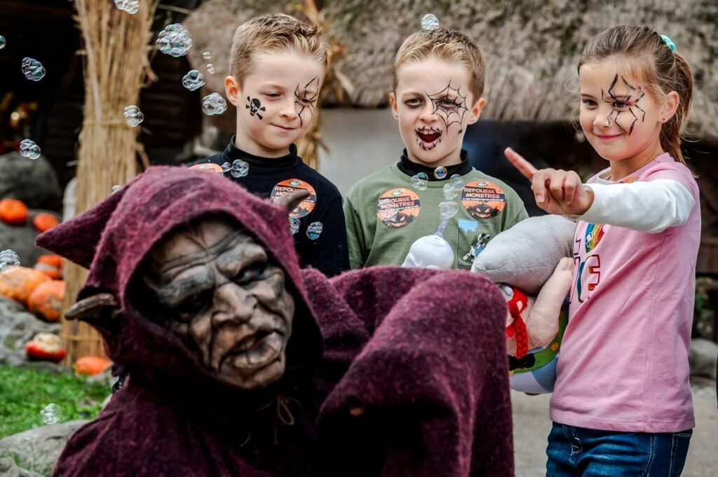 Trois enfants maquillés pour Halloween rient face à une créature encapuchonnée au masque ridé, au Parc Astérix
